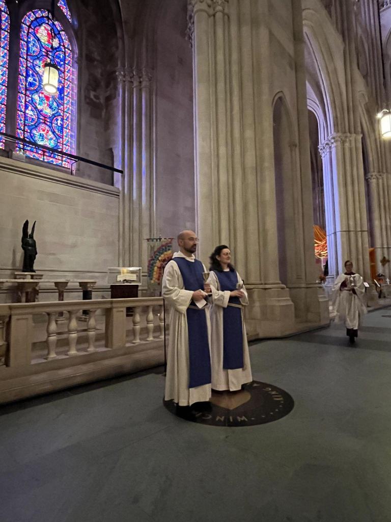Two members of the Society in white habits and blue scapulars stand in the nave of the Cathedral of Saint John the Divine.